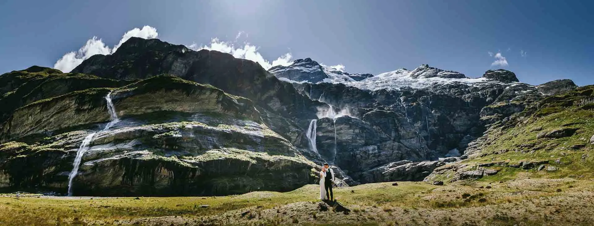 A bride and groom in the glacier-carved Earnslaw Burn valley, ringed by waterfalls and hanging glaciers near Queenstown