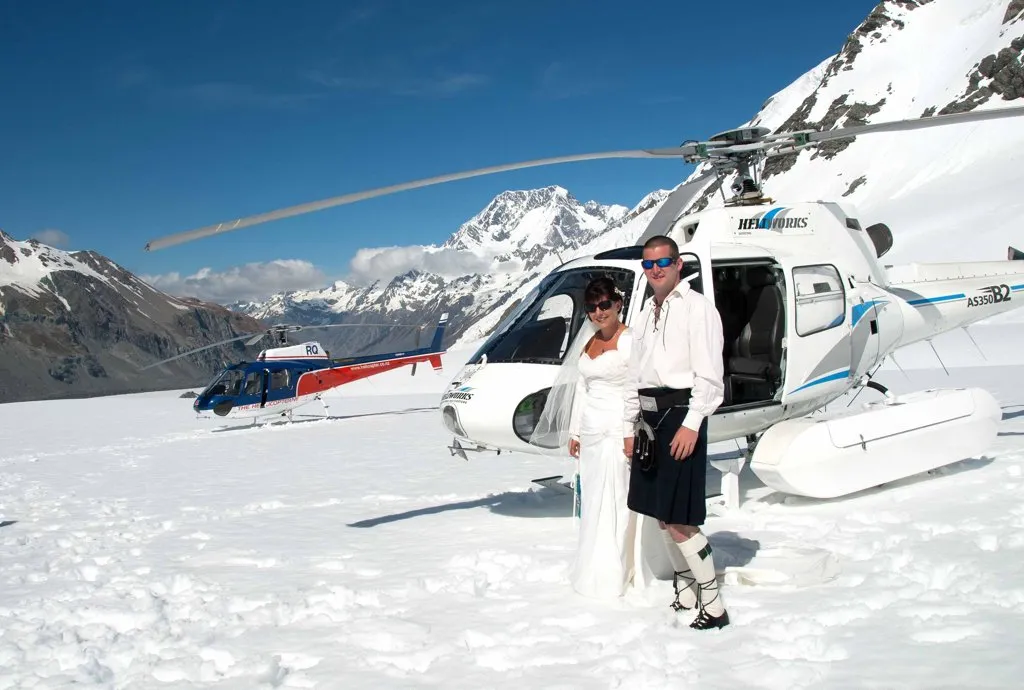 A bride and groom beside the helicopter on Richardson Glacier, Aoraki / Mt Cook rising behind